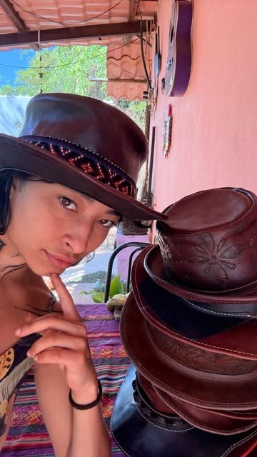 A leather hat being worn, beside a stack of finished hats.