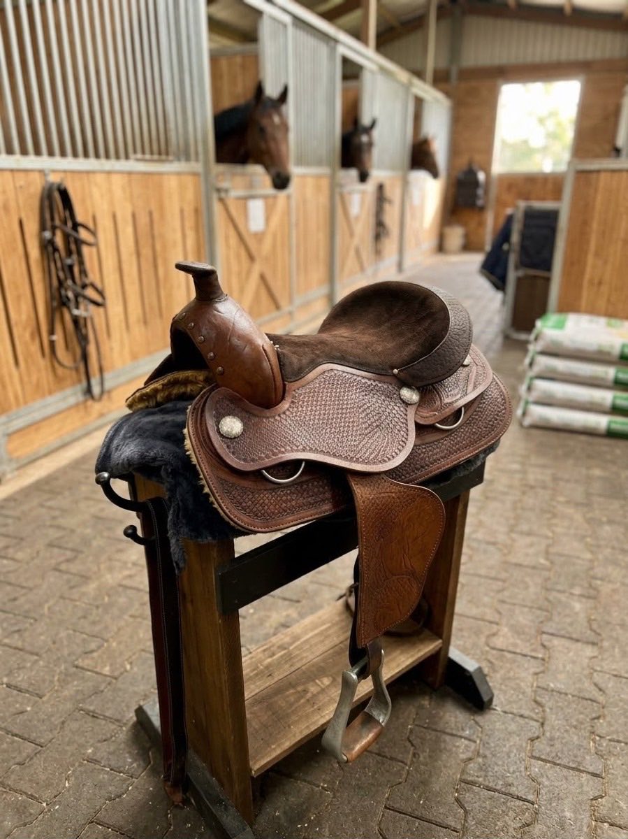 A western saddle with basketweave tooling on a stand inside the stable.
