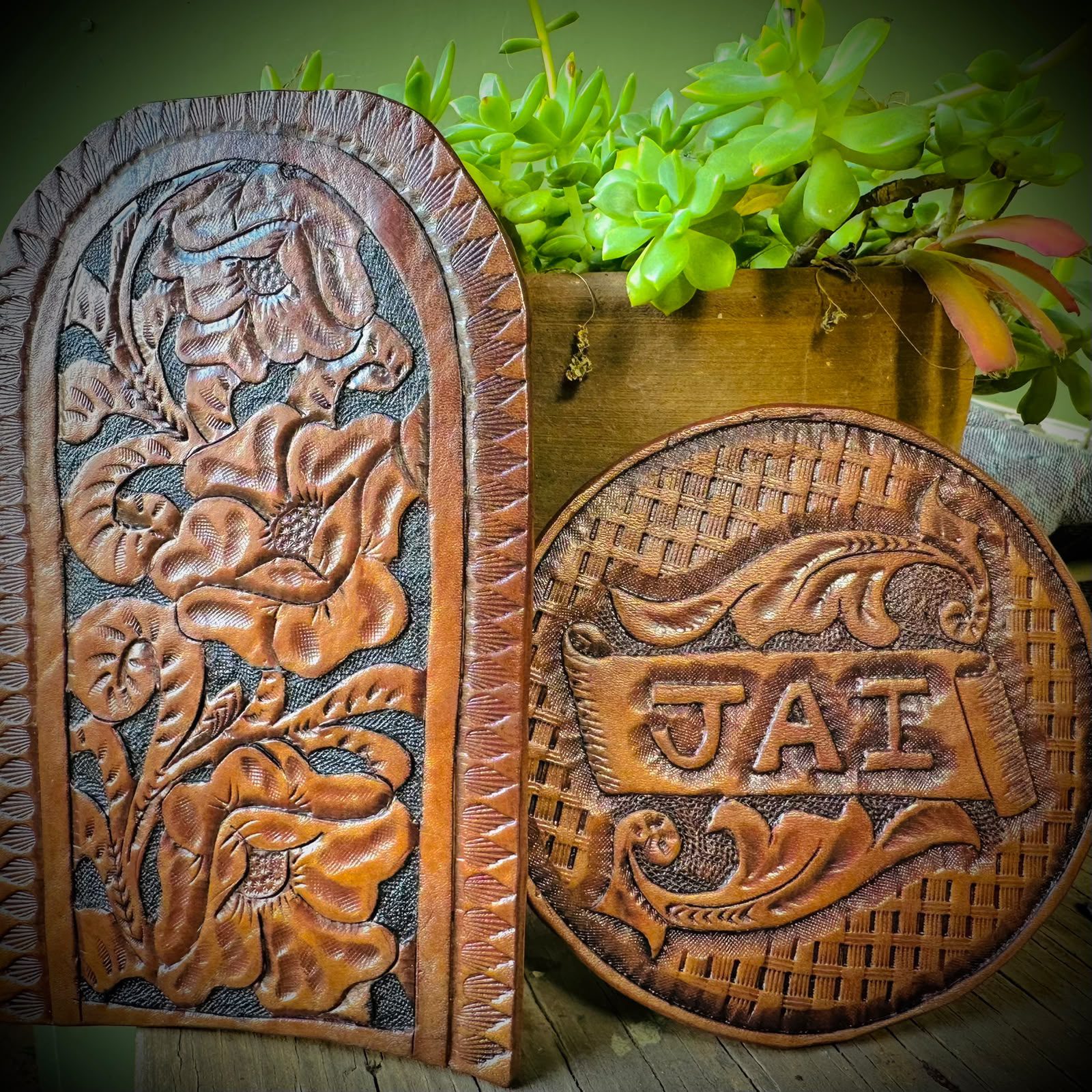 A tooled leather panel of flowers beside a round medallion reading JAI in relief.