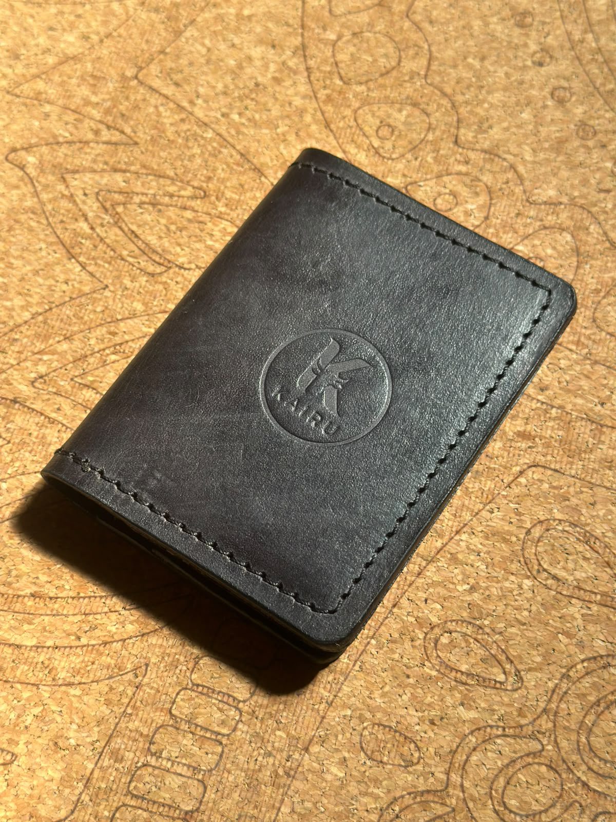 A closed Kaíru wallet in black leather, the K crest stamped in relief.
